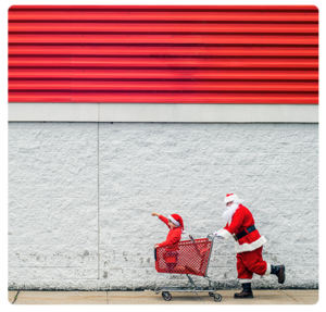 Photo d'un homme déguisé en père Noël poussant un caddie avec un enfant déguisé en père Noël se tenant debout à l'intérieur du caddie
