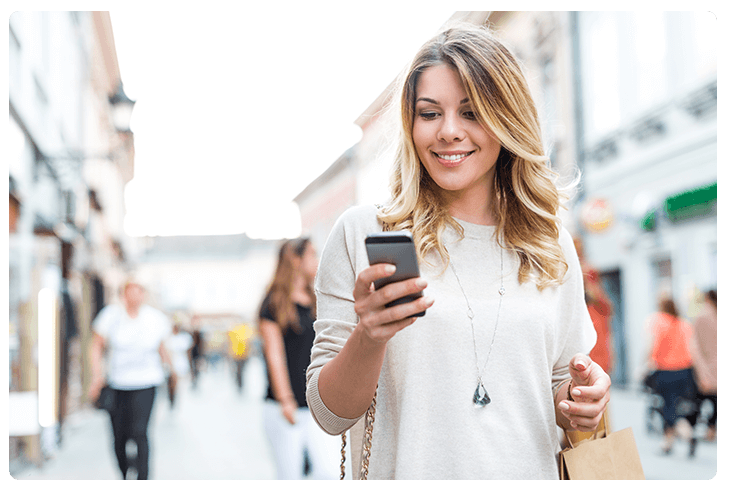 Photo d'une femme dans la rue consultant les avantages de son programme de fidélité sur son smartphone