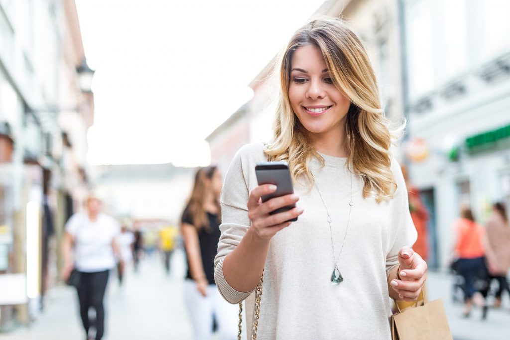 Photo d'une femme souriante dans la rue, regardant l'écran de son smartphone